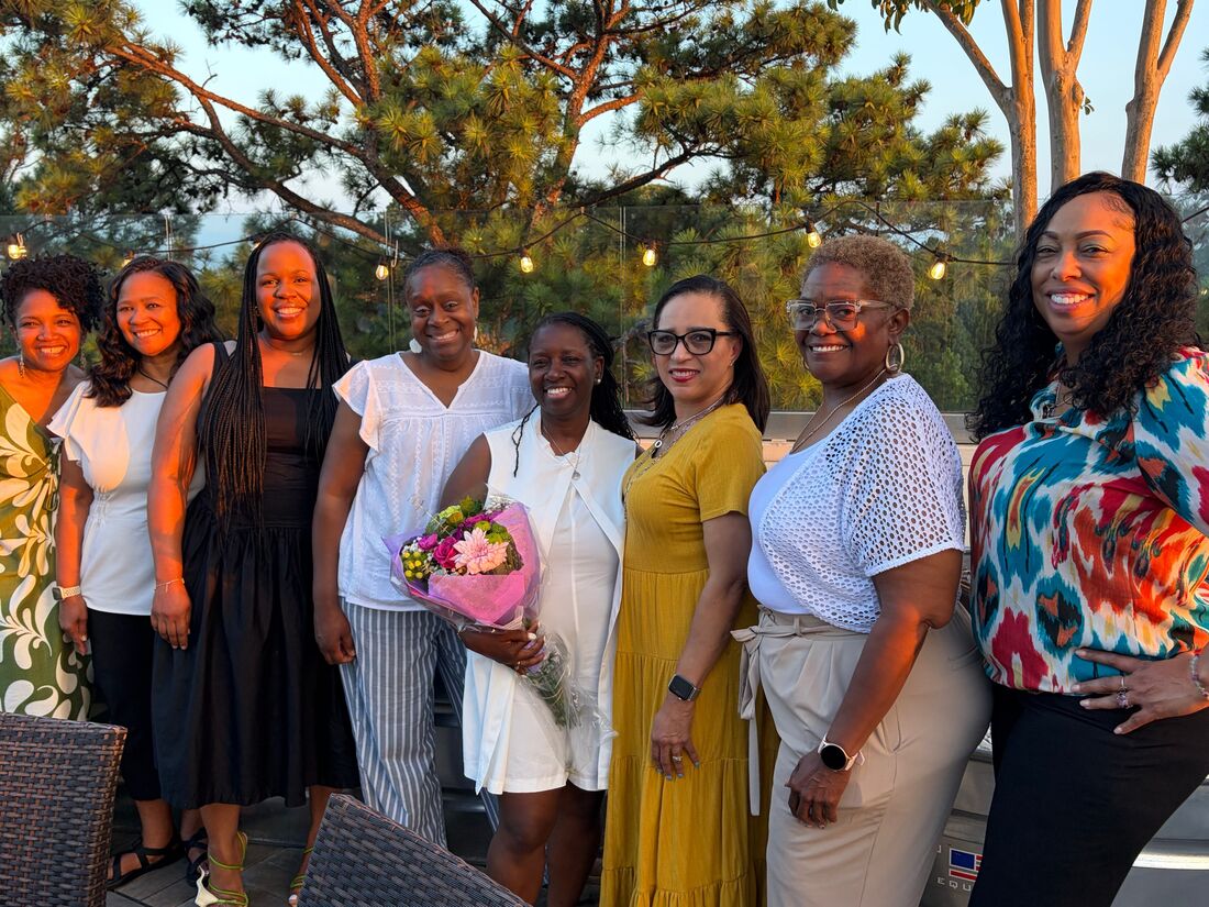 Women smiling together on a rooftop terrace at sunset, one holding flowers