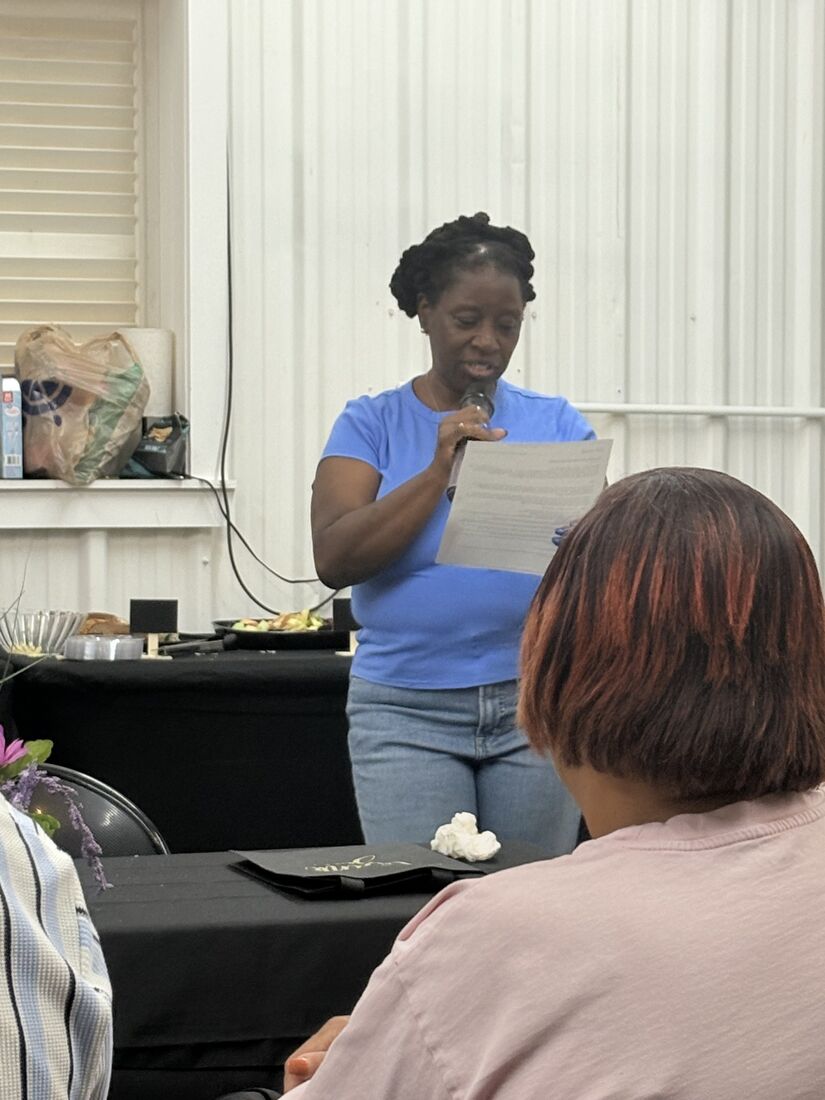 Wander Franklin reading from a page into a microphone to guests seated at tables at her launch event
