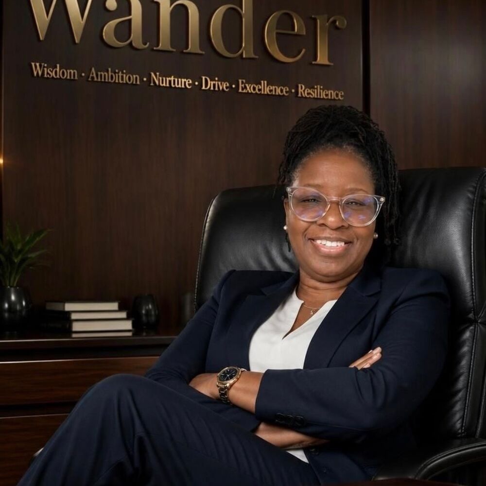 Wander Franklin in a navy suit, seated in a leather chair with her arms crossed, in front of a wood wall lettered Wander.